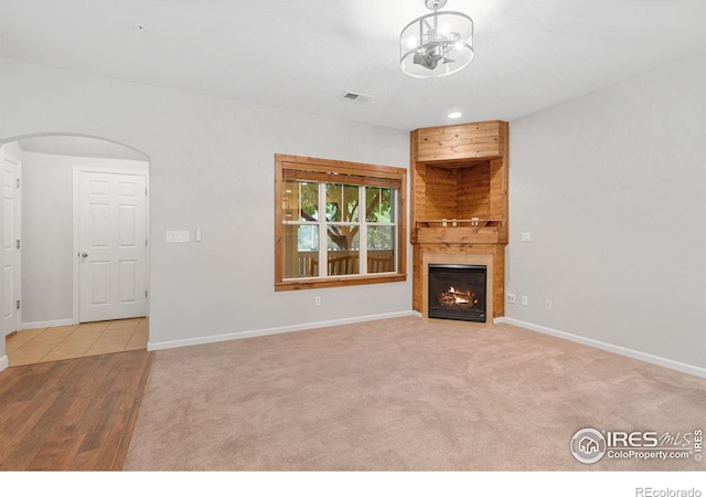 unfurnished living room featuring arched walkways, a glass covered fireplace, baseboards, and carpet flooring