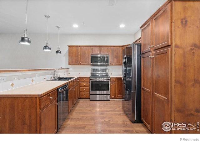 kitchen featuring stainless steel appliances, a sink, wood finished floors, brown cabinets, and recessed lighting