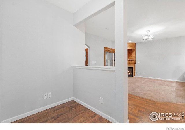 unfurnished room featuring wood finished floors, baseboards, a large fireplace, and a chandelier