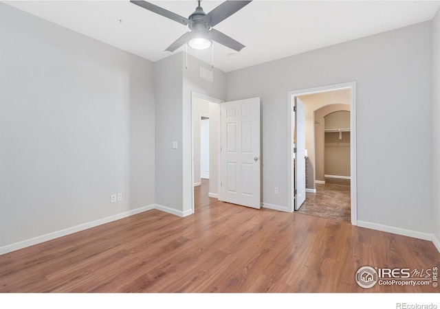 unfurnished bedroom featuring wood finished floors, baseboards, and arched walkways