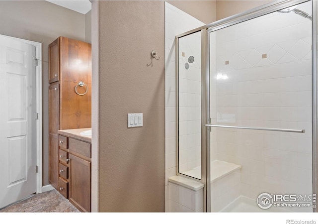 bathroom featuring a shower stall, a textured wall, and vanity