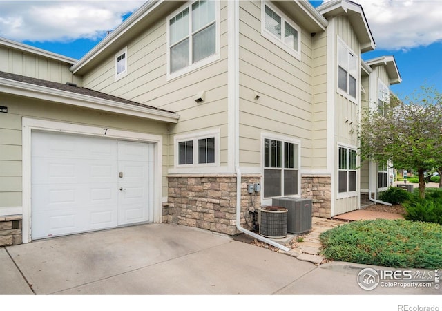 3639 29th St Unit 7, Greeley, CO 80634 - view of side of home with stone siding, concrete driveway, cooling unit, and board and batten siding