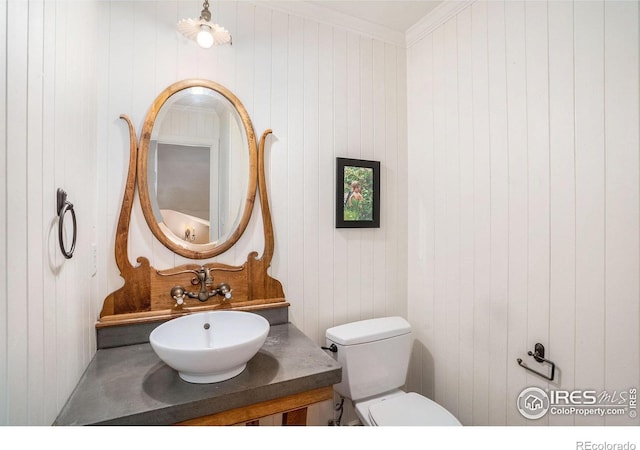 bathroom featuring toilet, wood walls, vanity, and ornamental molding