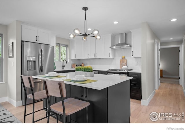kitchen featuring wall chimney range hood, white cabinets, light countertops, a kitchen island, and a breakfast bar