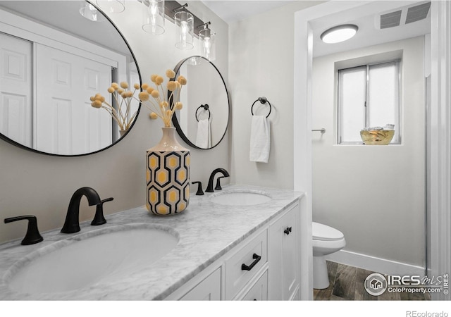 bathroom with toilet, wood finished floors, double vanity, and baseboards