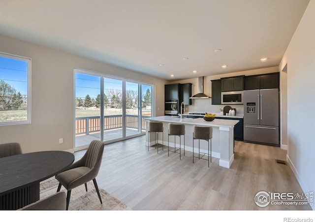 2710 Crystal Spgs, Longmont, CO 80503 - kitchen featuring stainless steel appliances, wall chimney range hood, light countertops, a center island with sink, and light wood-style floors