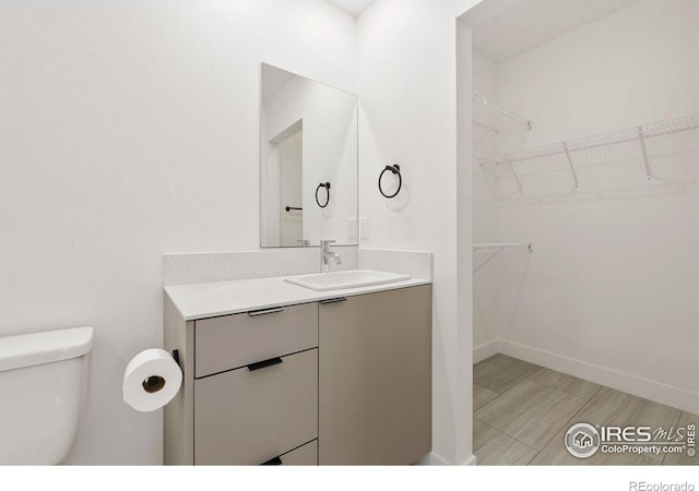 7864 5th St, Wellington, CO 80549 - bathroom featuring vanity, toilet, a walk in closet, and baseboards
