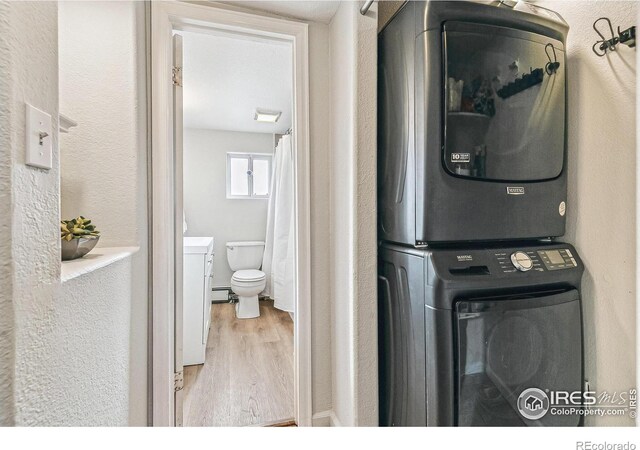 1970 Willow St, Denver, CO 80220 - clothes washing area featuring stacked washer / drying machine, wood finished floors, a baseboard heating unit, and a textured wall