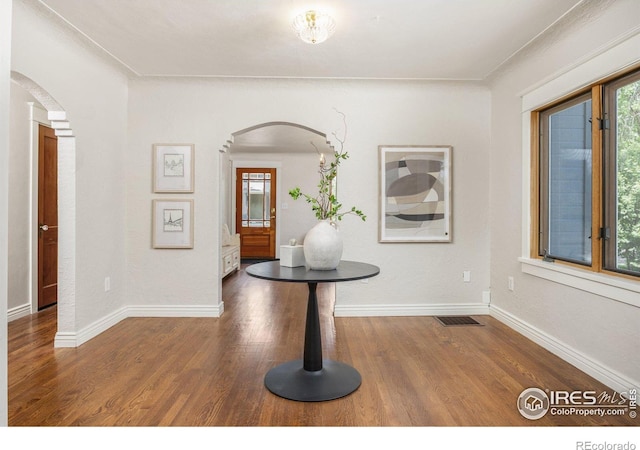 corridor featuring arched walkways, plenty of natural light, and wood finished floors