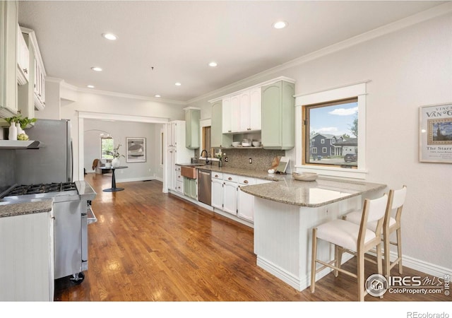 kitchen with appliances with stainless steel finishes, a peninsula, crown molding, tasteful backsplash, and light stone counters
