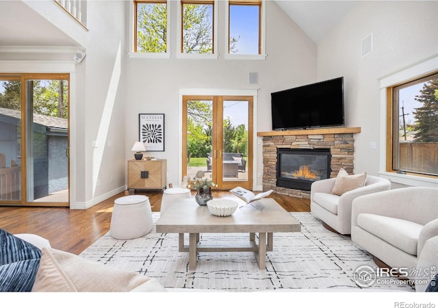 living area with wood finished floors, high vaulted ceiling, a stone fireplace, and baseboards