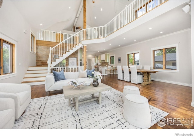living area featuring stairs, wood finished floors, a towering ceiling, baseboards, and crown molding