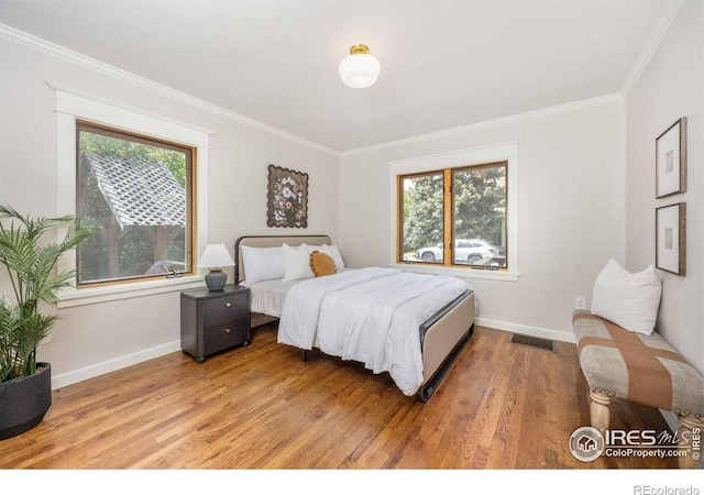 bedroom featuring ornamental molding, baseboards, multiple windows, and wood finished floors