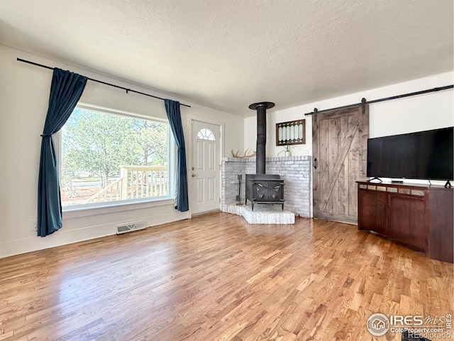 unfurnished living room featuring wood finished floors, a textured ceiling, a wood stove, and baseboards