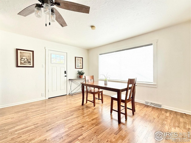 dining area featuring light wood-type flooring, a textured ceiling, baseboards, and ceiling fan