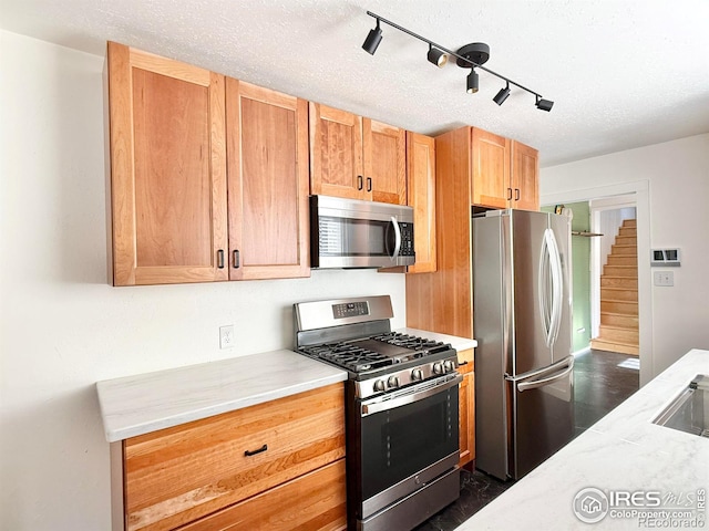 kitchen featuring appliances with stainless steel finishes, rail lighting, light stone counters, and a sink
