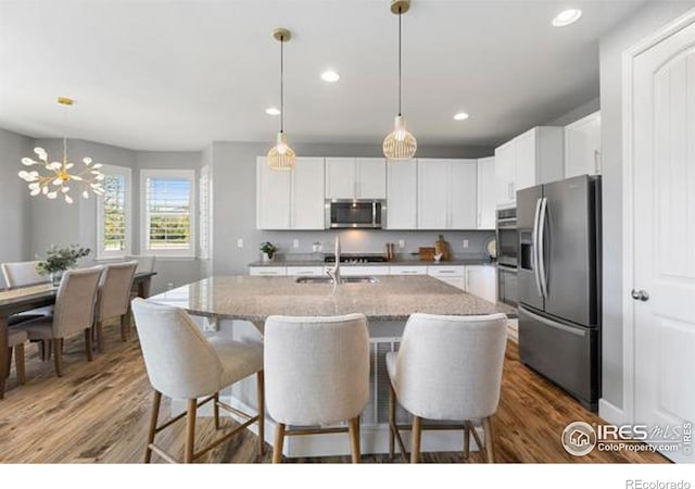 kitchen with stainless steel appliances, wood finished floors, a breakfast bar, light stone countertops, and an island with sink