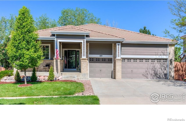 489 Hayloft Way, Brighton, CO 80601 - view of front of property featuring an attached garage, driveway, brick siding, a tiled roof, and a front lawn