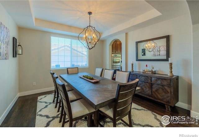489 Hayloft Way, Brighton, CO 80601 - dining space with a chandelier, arched walkways, a raised ceiling, dark wood-style flooring, and baseboards