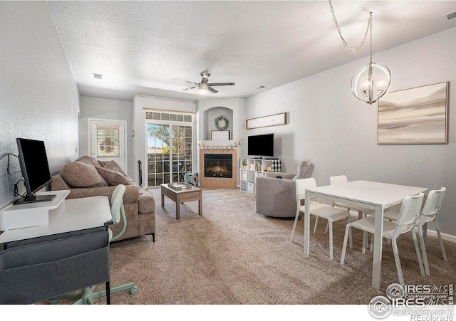 living area with carpet, ceiling fan, a glass covered fireplace, and a chandelier