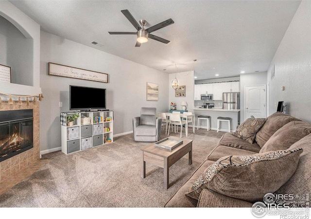 living area with carpet, a ceiling fan, and a tile fireplace