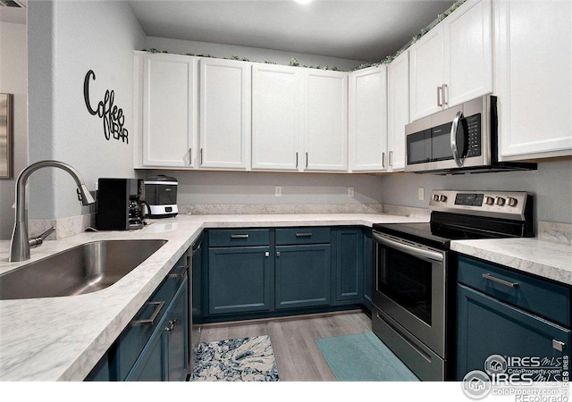 kitchen with appliances with stainless steel finishes, blue cabinets, a sink, and white cabinets