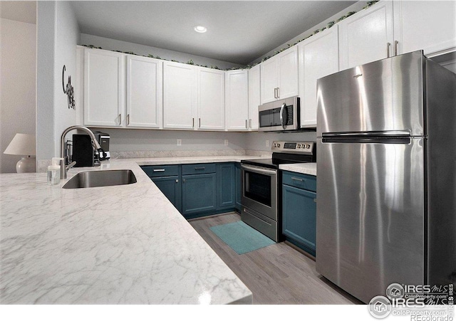 kitchen featuring stainless steel appliances, a sink, blue cabinets, wood finished floors, and recessed lighting