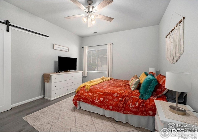 bedroom featuring a barn door, wood finished floors, baseboards, and ceiling fan