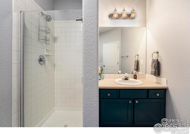 full bathroom with tiled shower, a textured wall, and vanity