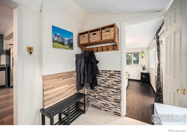 mudroom featuring a wood stove, lofted ceiling, wainscoting, and tile patterned flooring