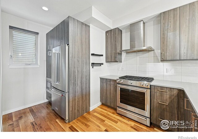 2625 W 25th Ave Unit 7, Denver, CO 80211 - kitchen featuring stainless steel appliances, wall chimney exhaust hood, decorative backsplash, light wood-type flooring, and light countertops