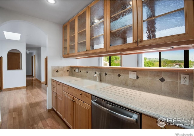 kitchen featuring stainless steel dishwasher, a sink, decorative backsplash, glass insert cabinets, and wood finished floors