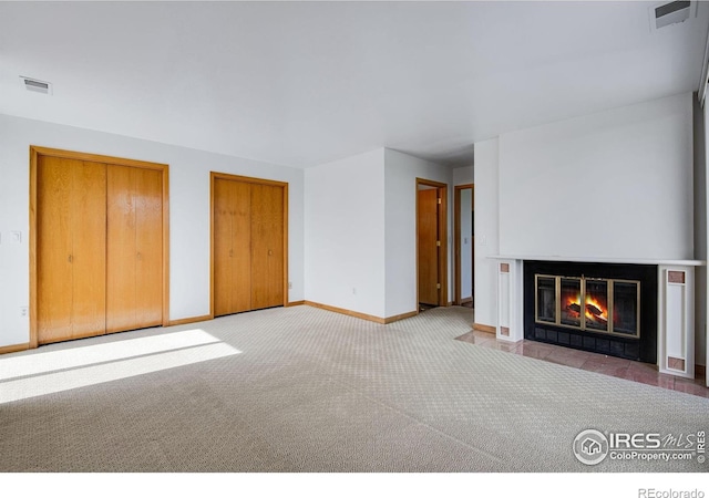 unfurnished living room featuring carpet flooring, baseboards, and a fireplace with flush hearth