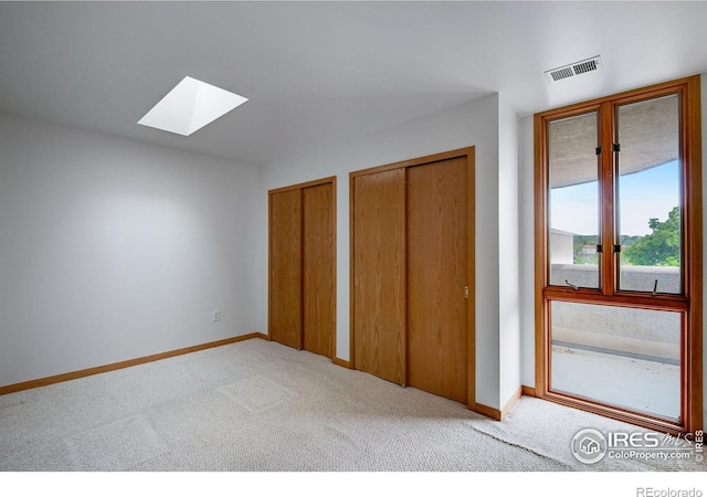 unfurnished bedroom with a skylight, carpet, two closets, and baseboards