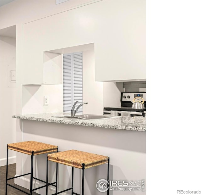 kitchen with stainless steel range with electric stovetop, a sink, white cabinetry, baseboards, and dark wood-type flooring