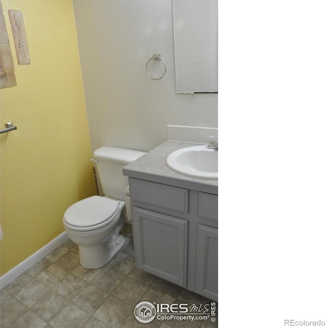 half bathroom featuring toilet, vanity, and baseboards