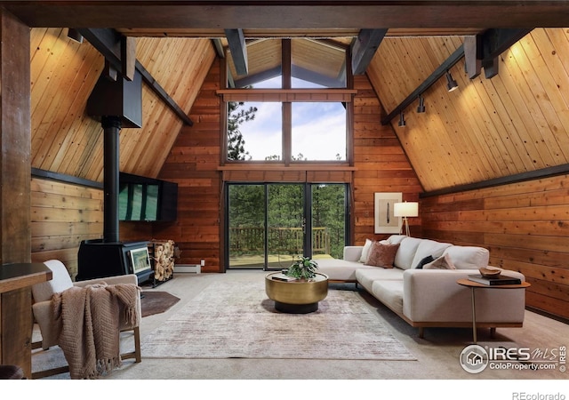carpeted living area featuring a wood stove, wood walls, beam ceiling, track lighting, and wooden ceiling