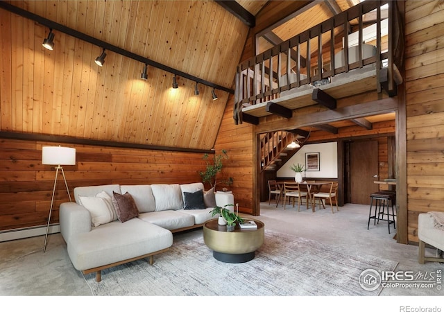 living room with carpet flooring, a baseboard heating unit, wood walls, rail lighting, and stairway