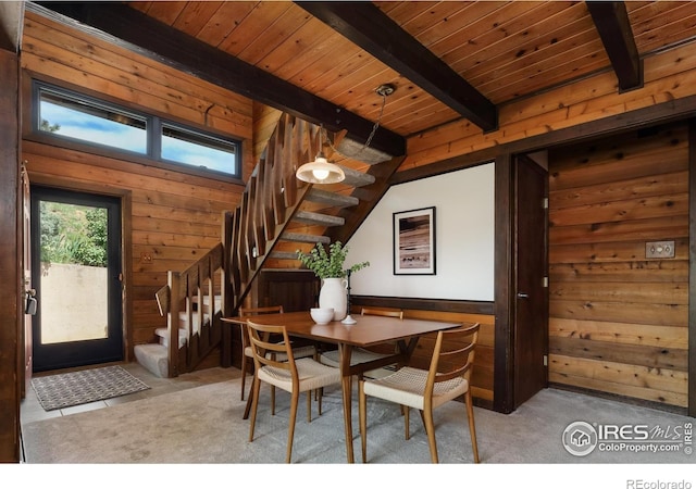 carpeted dining space featuring stairway, beam ceiling, wooden walls, and wood ceiling