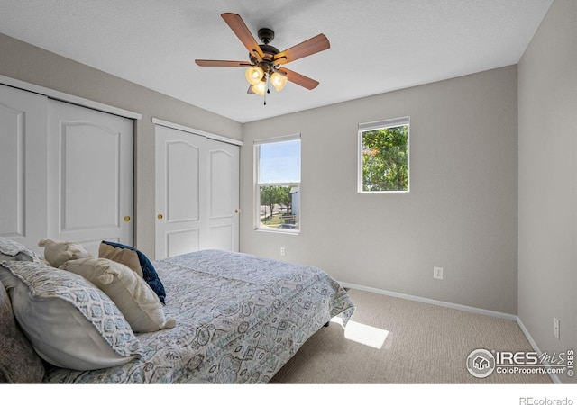 bedroom with baseboards, carpet flooring, multiple closets, and a ceiling fan