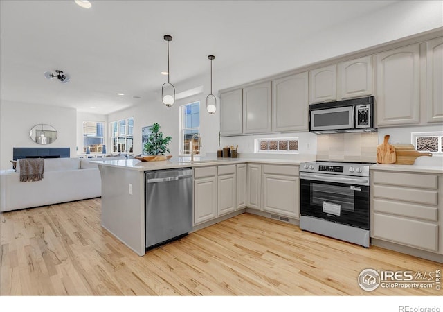 kitchen featuring appliances with stainless steel finishes, open floor plan, a peninsula, light wood finished floors, and light countertops
