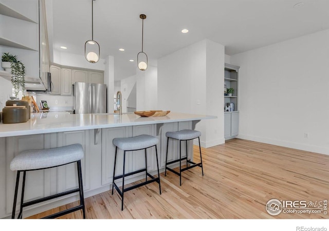 kitchen featuring freestanding refrigerator, open shelves, a peninsula, light wood-style flooring, and a breakfast bar area