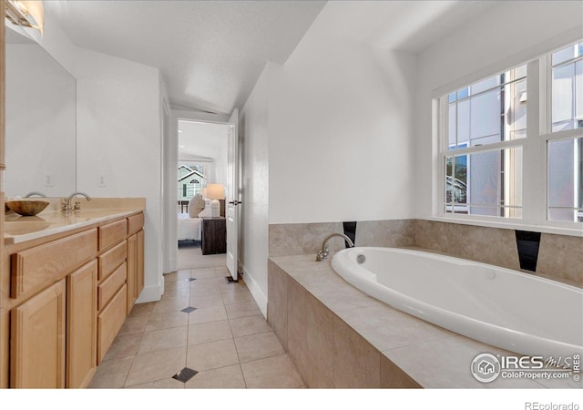 ensuite bathroom with tile patterned flooring, a bath, vanity, and baseboards