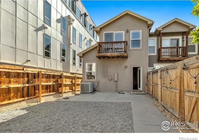 rear view of house with central air condition unit, a balcony, stucco siding, and a fenced backyard