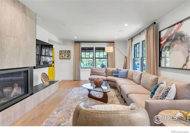 living area featuring wood finished floors, recessed lighting, baseboards, and a glass covered fireplace