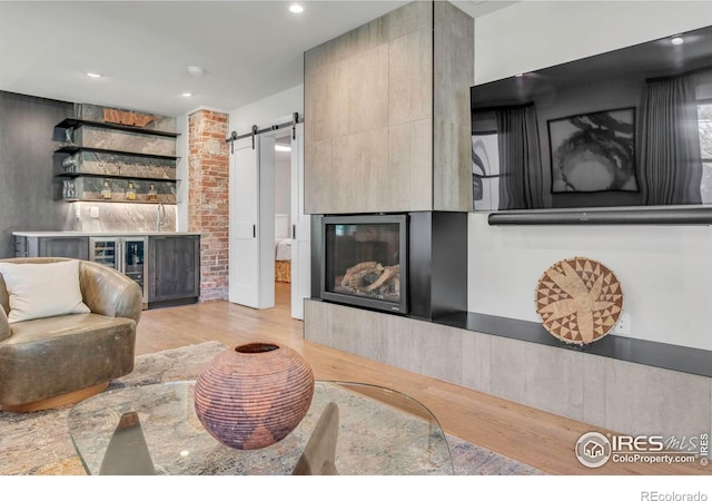 living area with a barn door, wood finished floors, and a glass covered fireplace