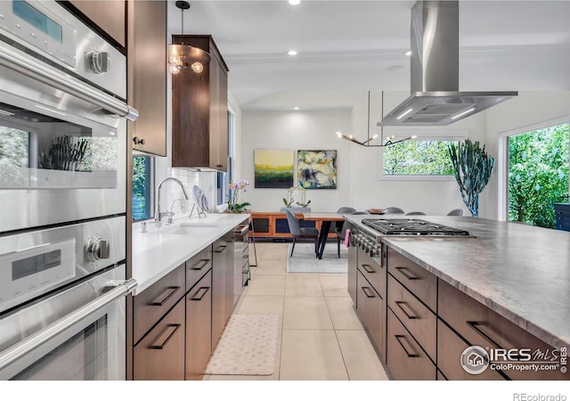 kitchen with stainless steel appliances, island exhaust hood, a sink, decorative light fixtures, and light tile patterned floors