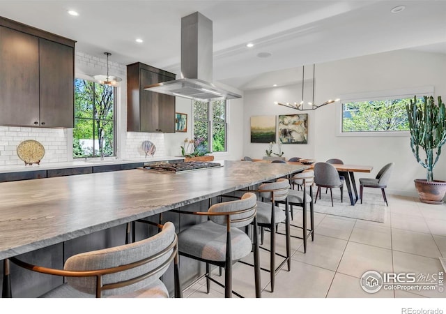 kitchen with island exhaust hood, dark brown cabinets, a kitchen breakfast bar, decorative backsplash, and light tile patterned floors