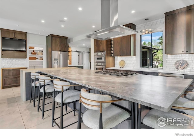 kitchen with appliances with stainless steel finishes, a barn door, island range hood, decorative backsplash, and recessed lighting