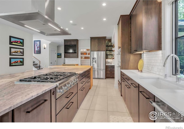 kitchen with appliances with stainless steel finishes, a sink, wall chimney exhaust hood, backsplash, and light tile patterned flooring